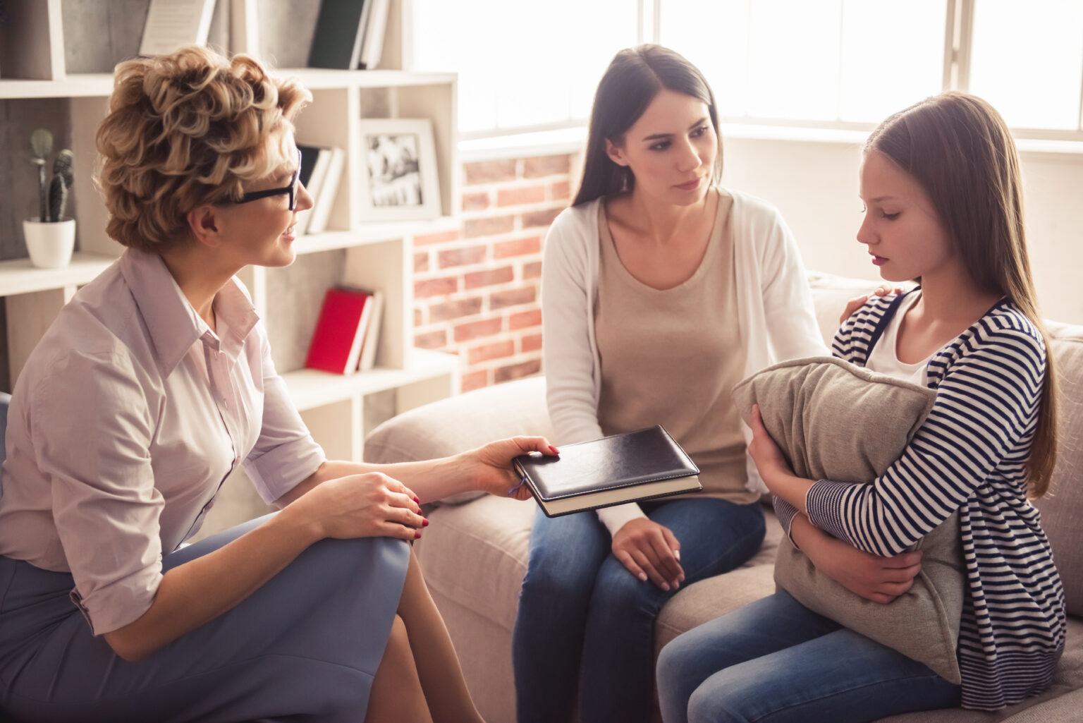 A therapist talking with a mother and her teenage daughter, who is holding a cushion