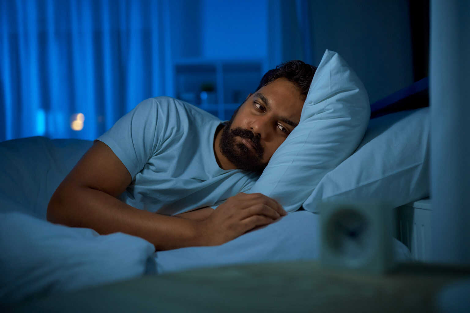 A man lying awake in bed at night, looking at the alarm clock beside him
