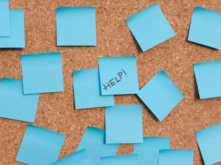 Turquoise sticky notes covering a cork board, one of them reading “HELP!”
