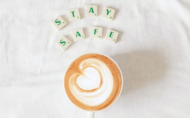 Overhead view of a latte with a heart in the foam, beside lettered tiles spelling “stay safe”
